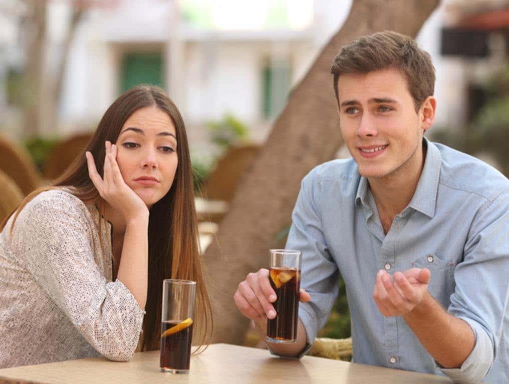 Man and woman dating in a restaurant terrace but she is boring while he speaks, cringeworthy date concept.