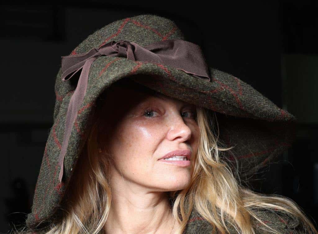 Pamela Anderson attends the Vivienne Westwood Womenswear Spring/Summer 2024 show facing right wearing a jacket and floppy hat.