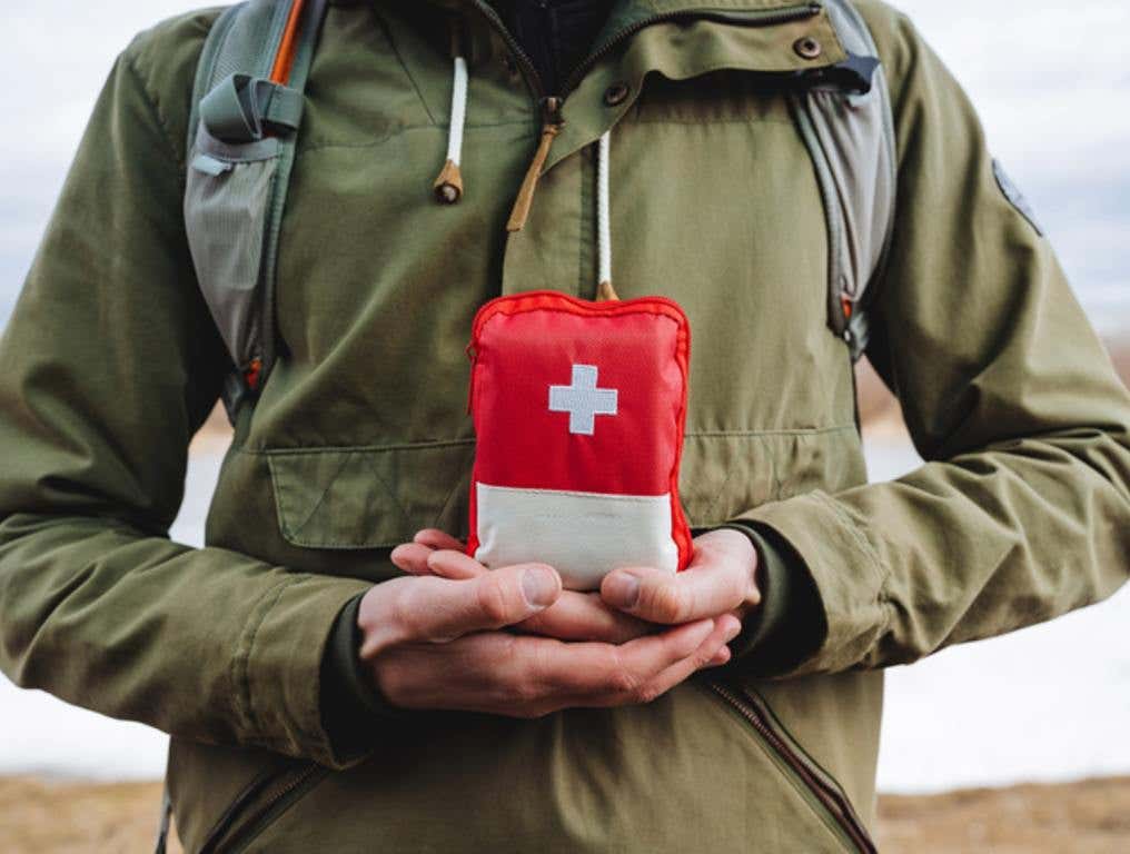 The guy holds in his hands a hiking bag, a first aid kit with medicines, a red emergency bag of first aid. Medicines in a package, red cross, travel safety concept