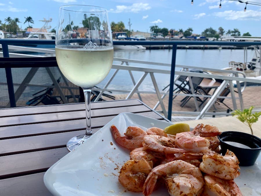 Glass of white wine witha plate of steamed shrimp and a waterfront background