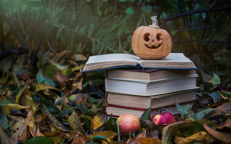 Colorful autumn scenery. Ripe Halloween carved pumpkin and a stack of old books on the background of fallen autumn yellow leaves in the garden