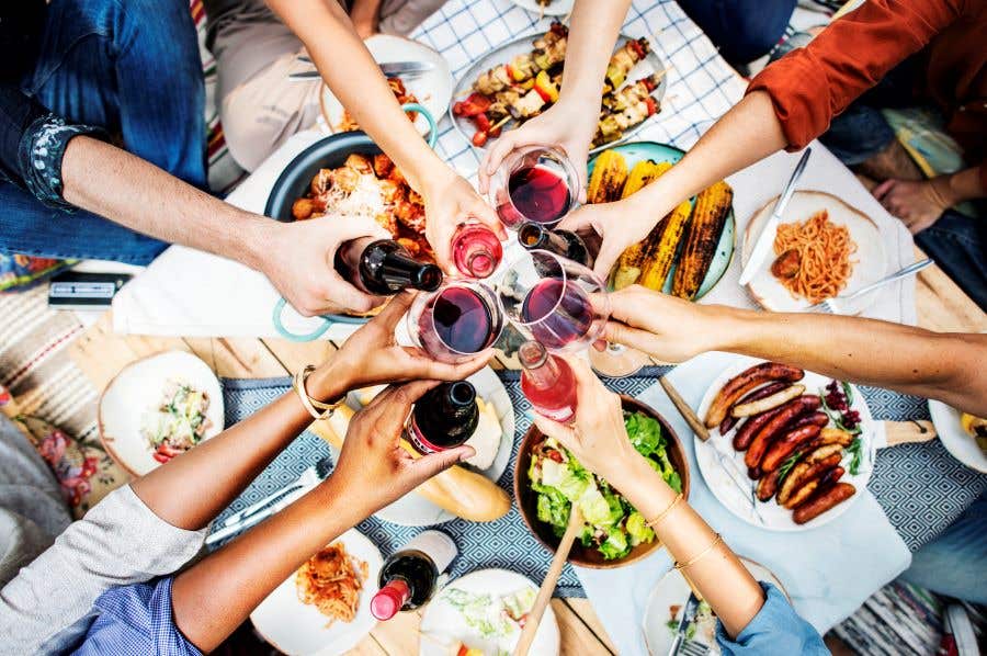 Table of food with 8 hands hold drinks raising them for cheers and exciting events in Southwest Florida for Sizzle Dining month