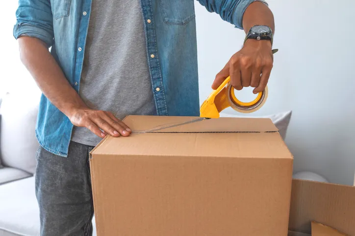 Close up of male hand packing cardboard box, concept moving house. House moving concept. Happy young couple moving into new apartment with packaging boxes. Male hands packing cardboard box with scotch. Charlotte County evacuations issued