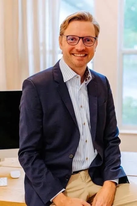 Man in a suit sitting on a desk and smiling as Innovations For Florida Attractions Are Out This Week